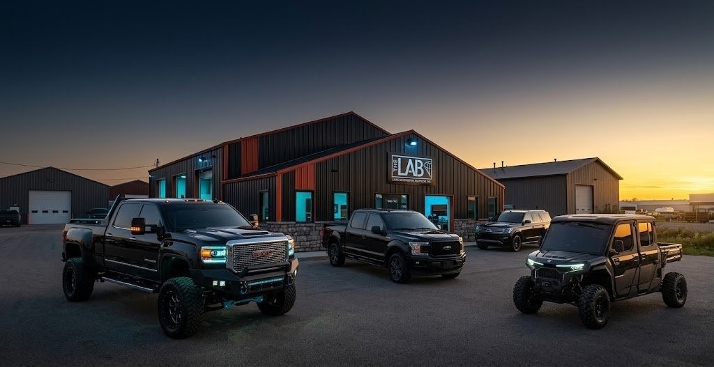 THE LAB shop at dusk with a lifted GMC, a Ford pickup, an SUV and a side-by-side parked out front