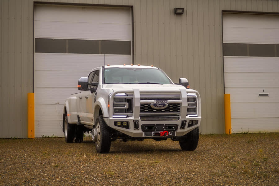 White Ford Super Duty dually with a Gridiron Full Tube winch bumper parked in front of a shop