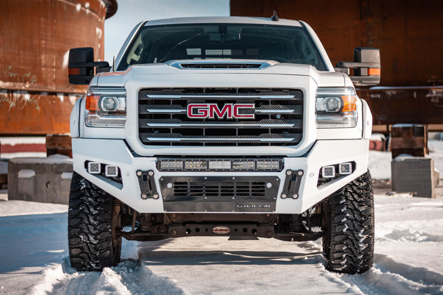 White GMC Sierra HD with a Gridiron Base front bumper and LED lights in the snow