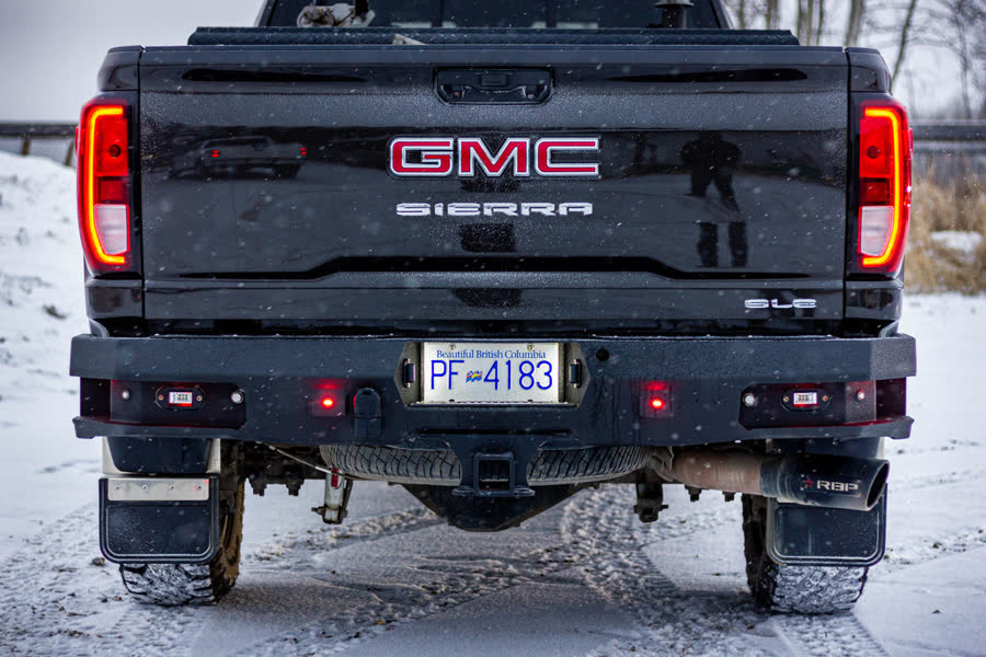 Rear of a black GMC Sierra with a Gridiron rear bumper in the snow